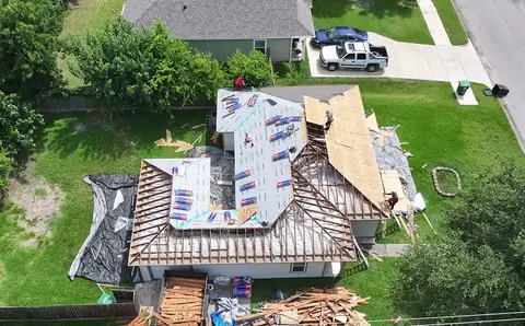 The same single-story home from above with rafters exposed on one side and new decking and underlayment on the other, and the crew at work