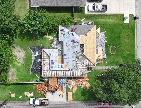 Single-story home seen from above with the roof open to the rafters on one side and new decking and underlayment on the other