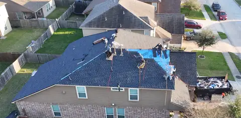 Crew installing dark shingles over the underlayment on the same two-story home