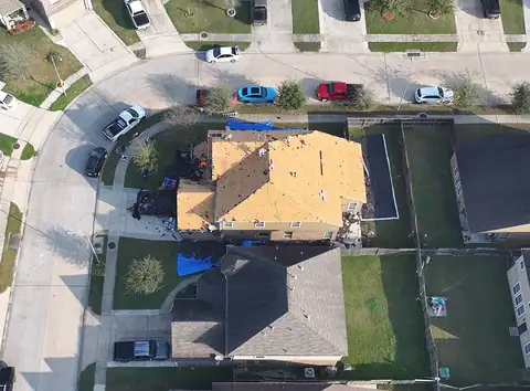 Two-story home from above with the old shingles removed and the roof decking exposed