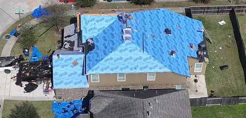 Blue synthetic underlayment covering the roof of the same two-story home, with the crew on the roof
