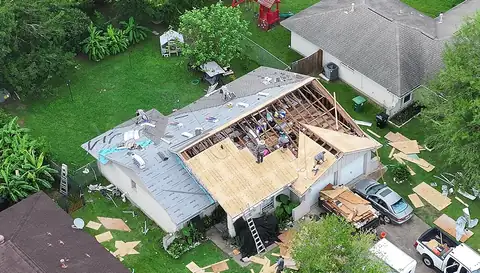Single-story home with one section of the roof open to the rafters while the crew installs new decking