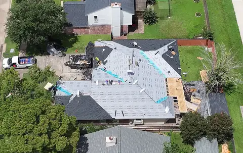 Single-story brick home from above with underlayment installed and the crew on the roof
