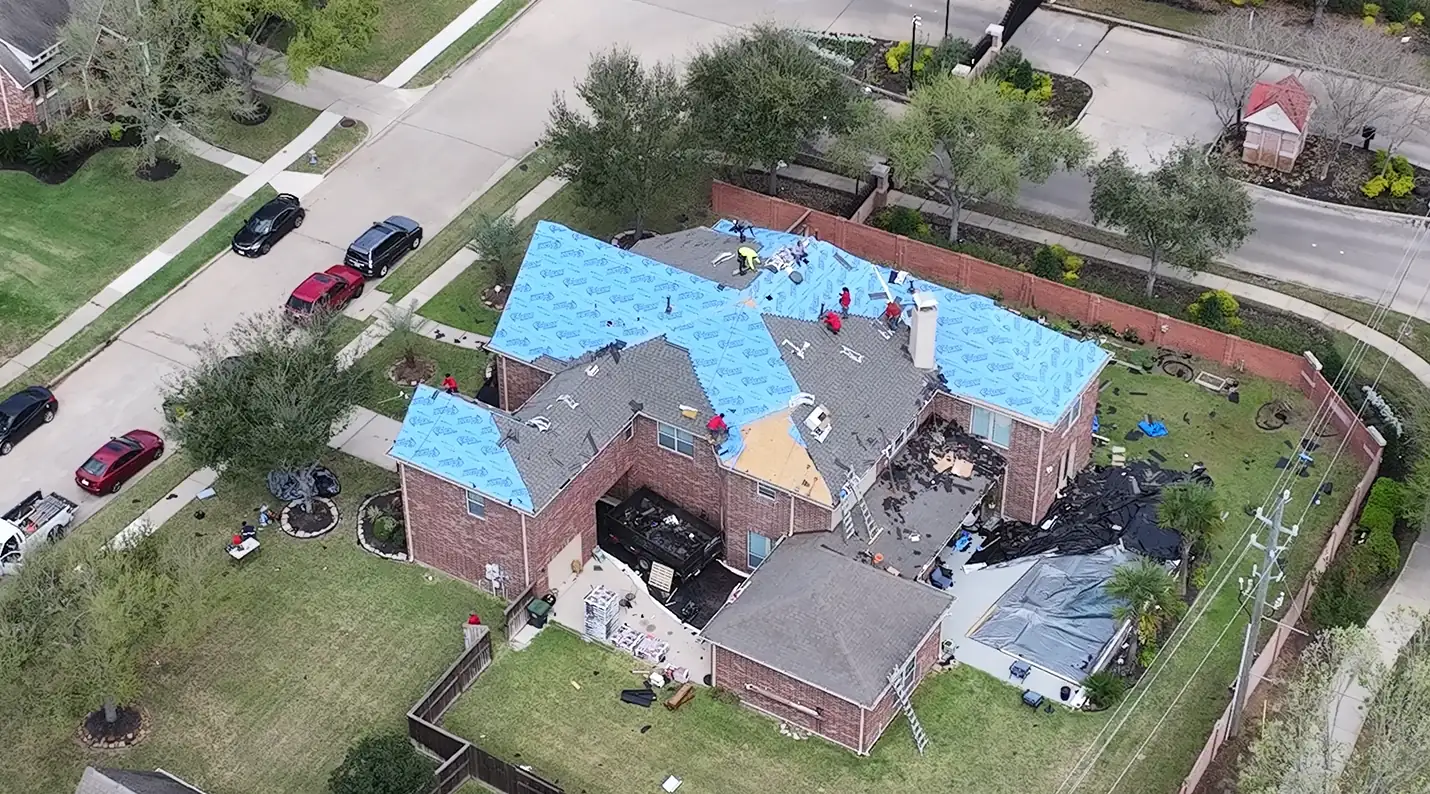 3 S Roofing crew installing underlayment and new shingles during a full roof replacement on a two-story brick home in the Houston area