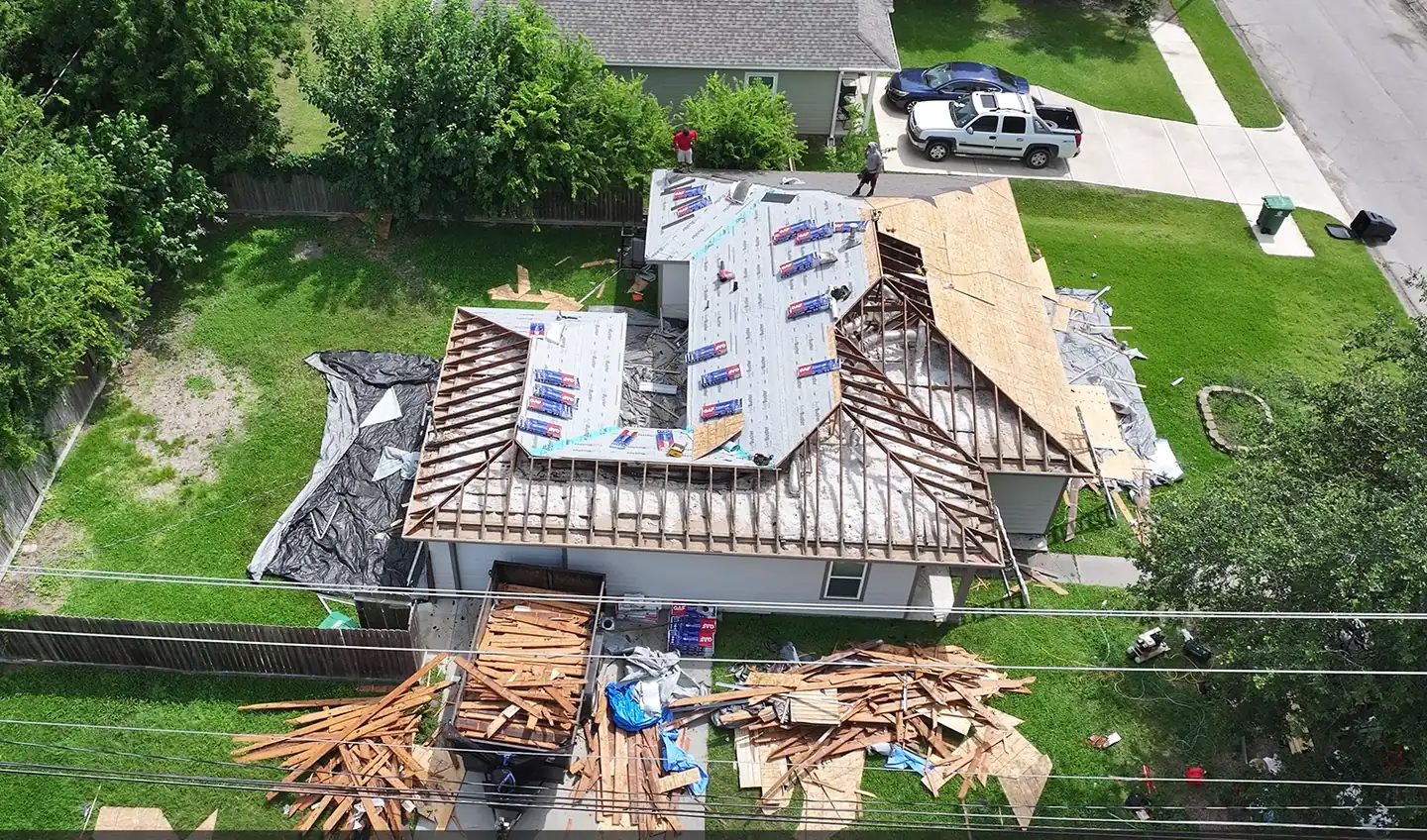 Drone view of a single-story home with the old roof removed down to the rafters, new decking and underlayment going on, and the crew at work