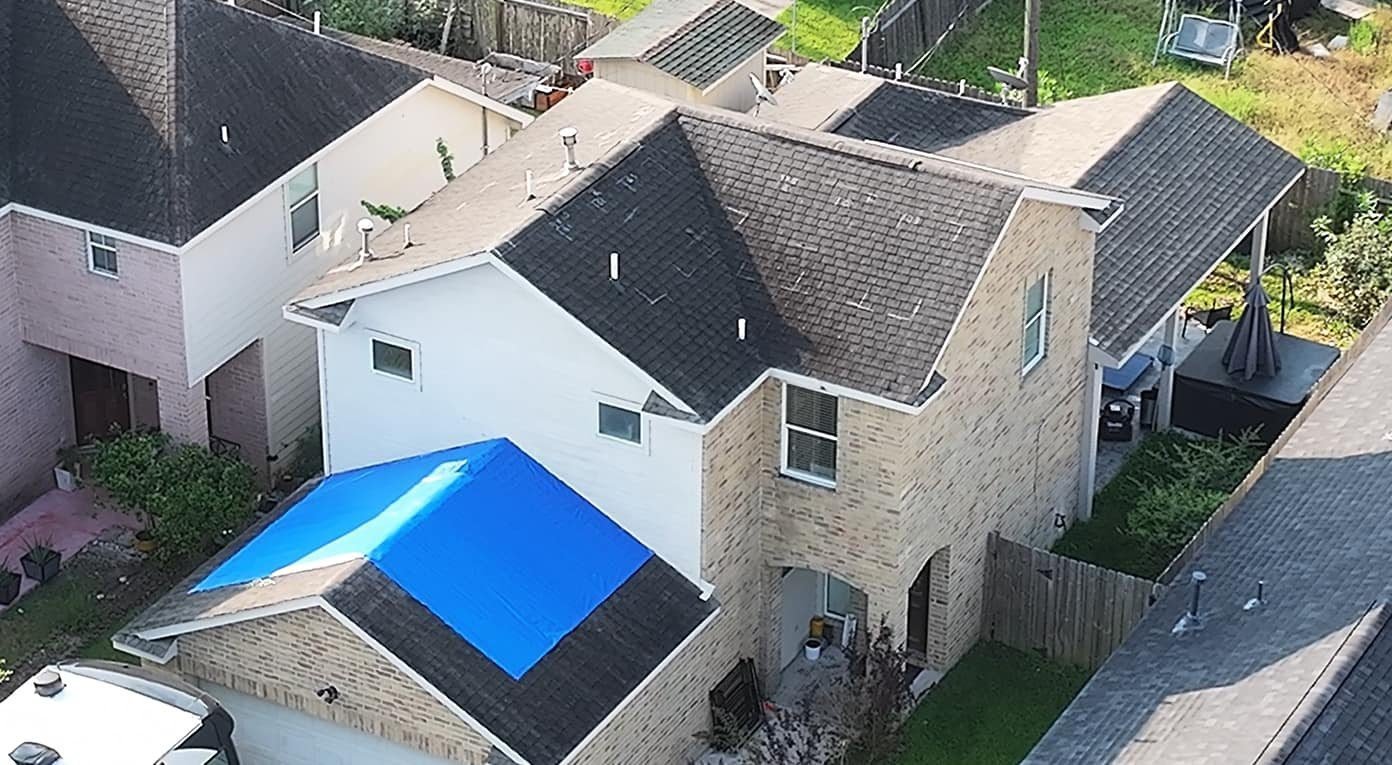 Two-story home with a temporary tarp over part of the roof and chalk inspection marks on the upper roof