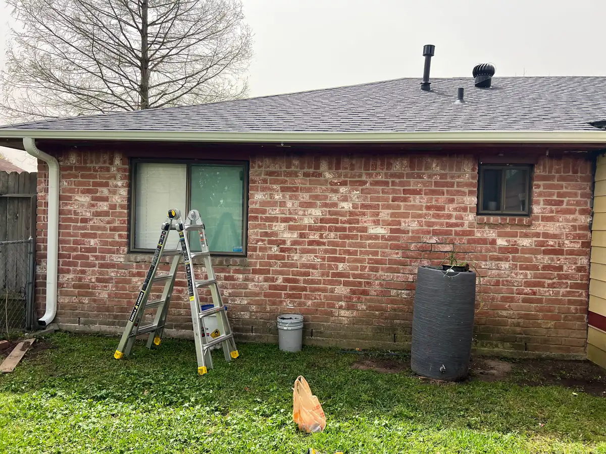 White gutter and downspout on a brick wall, with a ladder set up during the work
