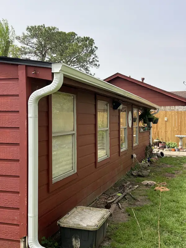 White gutter and downspout along the side of a red siding home
