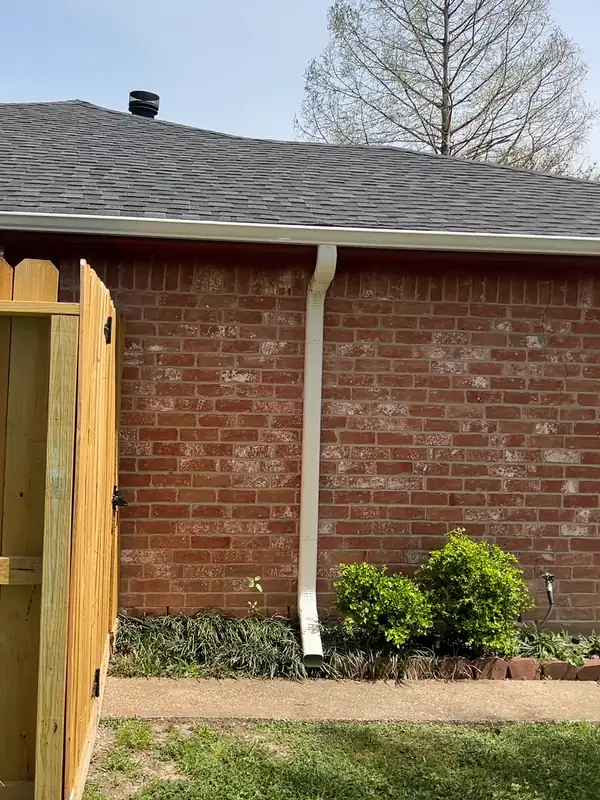 New wood fence gate next to a white downspout on a brick home